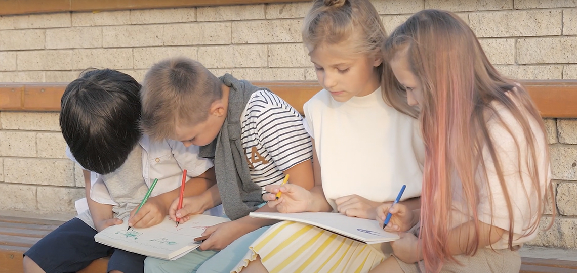 4 children sitting on bench outside school writing in notebooks